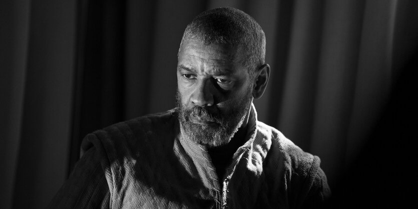 Denzel Washington als Macbeth mit viel Schatten vor einem Vorhang.