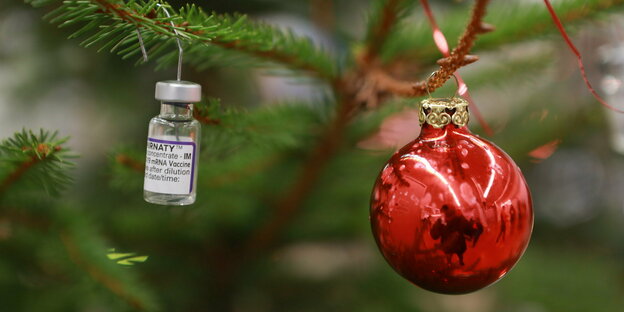 Impfdose hängt neben einer Weihnachtsbaumkugel am Baum