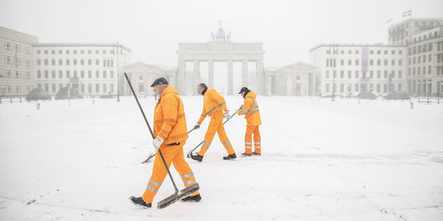 Orange gekleidete Männer der Berliner Stadtreinigung gehen vor dem Brandenburger Tor im Schnee
