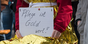 Eine Frau trägt während der Kundgebung zum 1. Mai 2018 in Braunschweig ein Schild "Pflege ist Gold wert!" in den Händen.