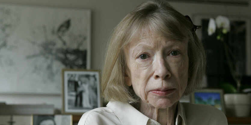 Joan Didion blickt in die Kamera. Sie ist eine alte Frau mit schmalem Gesicht und hellen, kinnlangen Haaren. Im Hintergrund stehen Bilder.