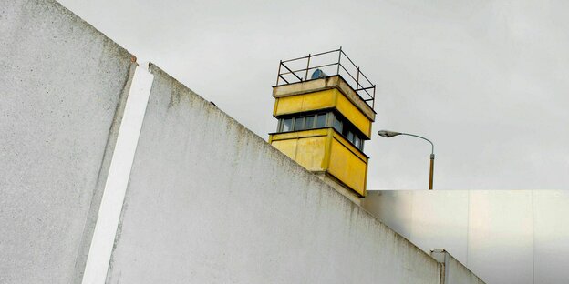Hinter der Resten der Berliner Mauer ragt ein ehemaliger Grenzschutzturm hervor
