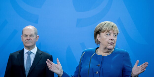 Olaf Scholz und Angela Merkel stehen vor einer blauen Wand