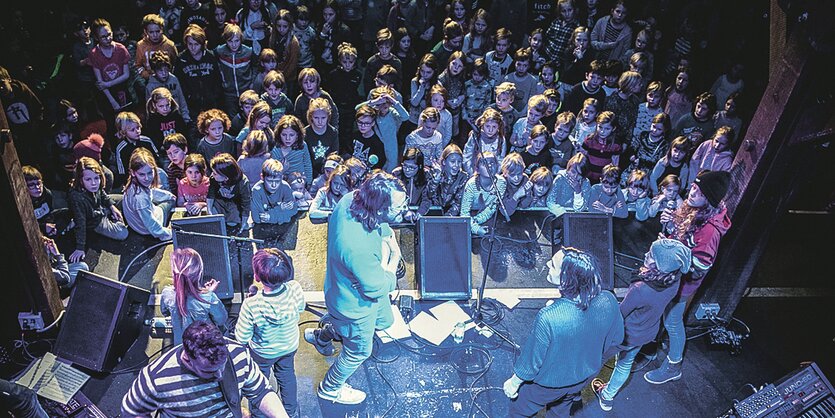 Musiker stehen auf einer Bühne, vor der Bühne stehen Kinder