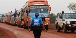 Eine Frau mit UNHCR-Shirt geht auf eine Schlange aus Bussen zu