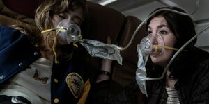 Zwei junge Frauen mit Sauerstoffmasken in einem Flugzeug