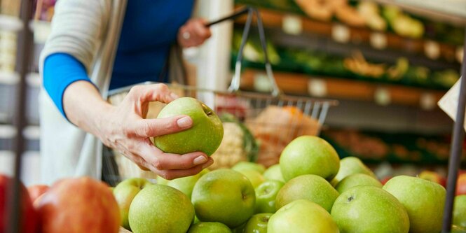 Eine Frau begutachtet einen Apfel im Bioladen