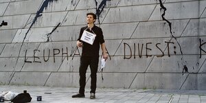 Henning Jeschke steht vor einer Wand auf der aufgesprüht steht: "Leuphana divest".