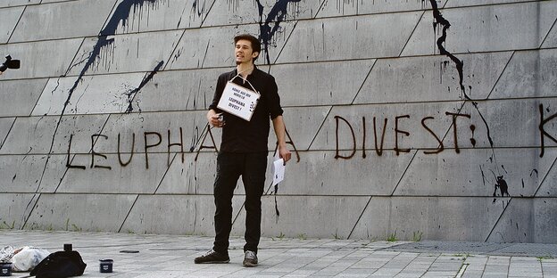 Henning Jeschke steht vor einer Wand auf der aufgesprüht steht: "Leuphana divest".