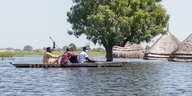 Menschen fahren mit einem Kanu durch ein überflutetes Gebiet.
