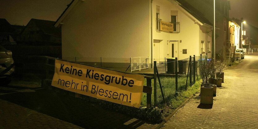 Ein Transparent hängt an einem Gartenzaun vor einem Einfamilienhaus in der Dämmerung: Keine Kiesgrube mehr in Blessem !