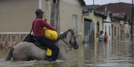 Mann reitet auf einem Pferd durch meterhoch überflutete Straße