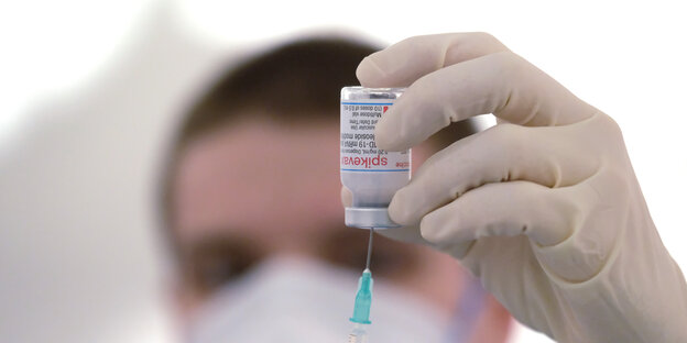 Ein Mediziner zieht eine Spritze an einer Flasche Impfstoff auf