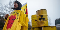 Eine Frau steht mit Atomkraft-nein-Danke-Poncho und einer entsprechenden Fahne vor radioaktiv markierten Fässern