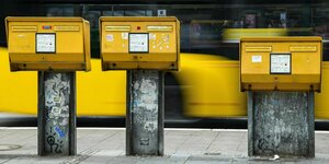 Drei gelbe Briefkästen an einer Straße.
