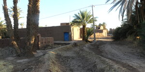 Eine Kasbah in der Wüste mit Palmen und Häusern hinter Mauern