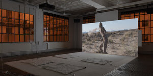 Filmprojektion in einer Industriehalle, zu sehen eine nackte Frau in wüstenartiger Landschaft