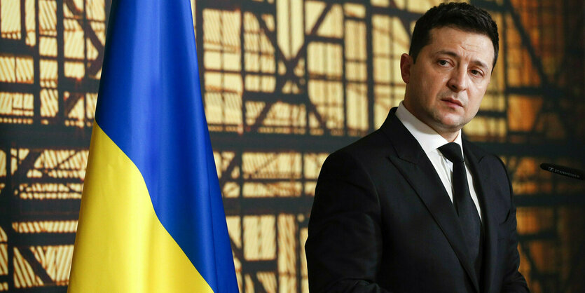 Wolodymyr Selenskyj steht neben einer Ukraine Flagge