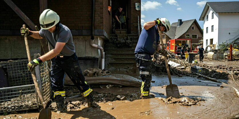 Feuerwehrmänner tragen mit Schaufeln mühsam Schlamm ab