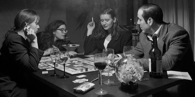 Drei schick gekleidetet Frauen und ein Mann sitzen an einem TIsch und spielen Monopoly