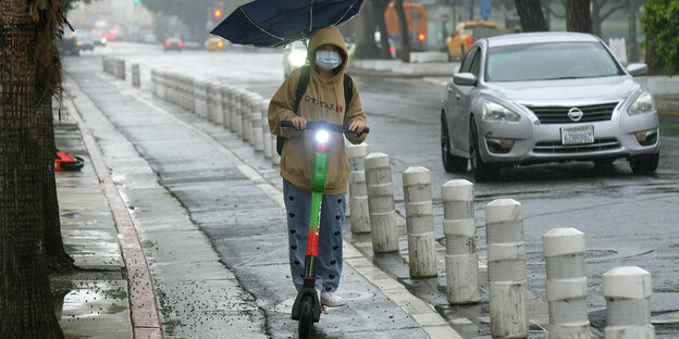 Ein Mann fährt mit Regenschirm auf einem E-Roller