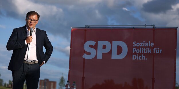 Der neue Ostbeauftrage Carsten Schneider mit Mikrofon vor einem Plakat der SPF - Soziale Politik für dich, steht dort