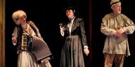 Eine Akkordeonspielerin, eine Frau mit Zylinder und Handy und ein Mann mit einfacher Mütze im Theaterstück "Auferstehung" am Berliner Ensemble