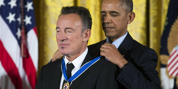 Barack Obama steht hinter Bruce Springsteen und hängt ihm eine Medaille um.