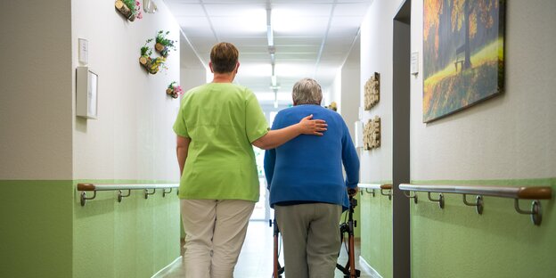 Eine Pflegefachkraft geht mit einer Bewohnerin durch ein Seniorenheim in Nienburg.