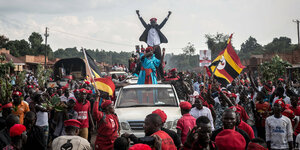 Oppositionsführer Bobi wine reckt die Hände in dei Höhe a, er steht auf einem Fahrzeug und ist umringt von Anhängern
