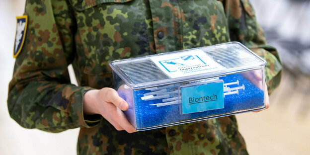 Eine Soldatin hält eine Kiste mit Biontech Spritzen in der Hand.
