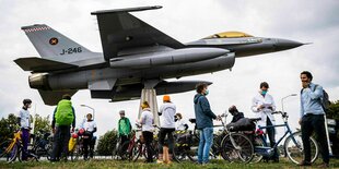 Aktivisten stehen mit einer gebastelten Rakete und Transparent unter einem Flugzeug