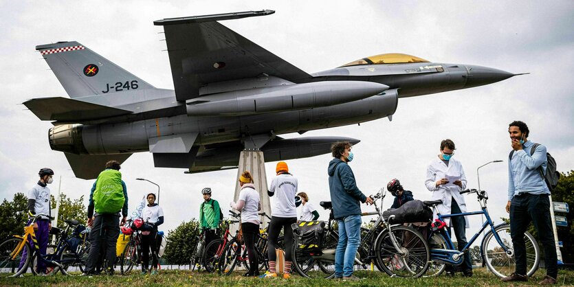 Aktivisten stehen mit einer gebastelten Rakete und Transparent unter einem Flugzeug