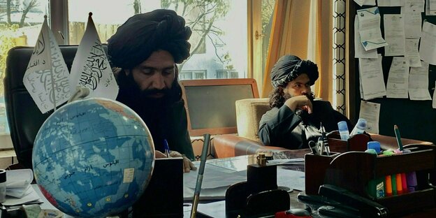 Zwei Taliban mit Turban sitzen hinter einem Schreibtisch
