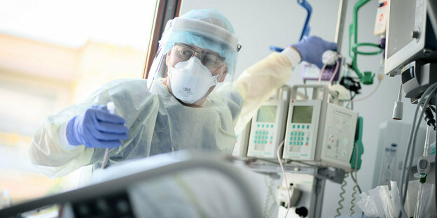 Ein Intensivpfleger mit Schutzanzug an einem Krankenbett