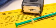 Eine Spritze liegt neben einem Impfstoffstempel des Impfzentrums Bremen auf einem gelben Impfausweis