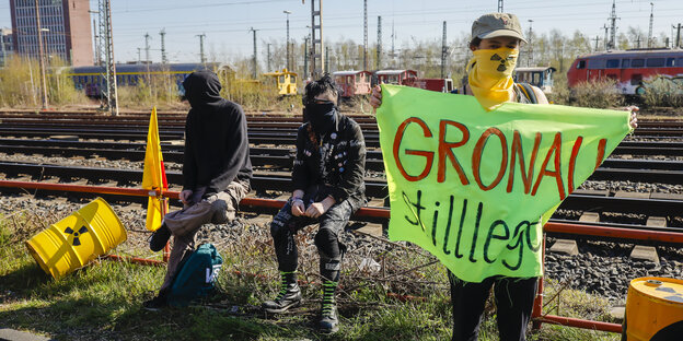 3 vermummte Demonstranten, einer hält ein grell grünes Transparent, "Gronau stillegen"