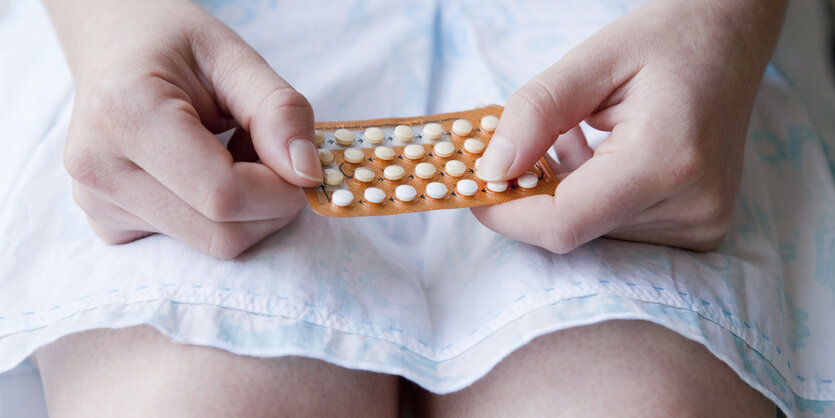 Eine junge Frau hält eine Pillenpackung in ihren Händen, sie trägt einen Sommerrock