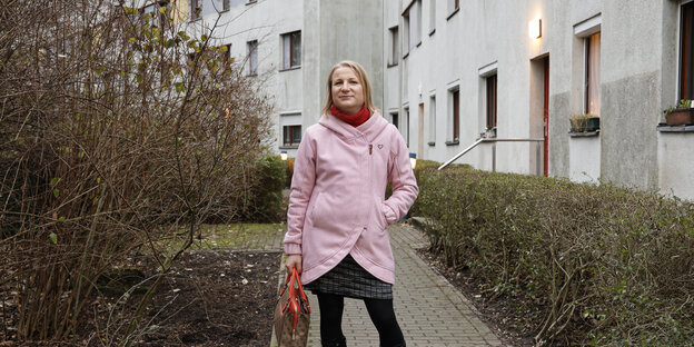 Person in rosa Mantel vor Häuserfront