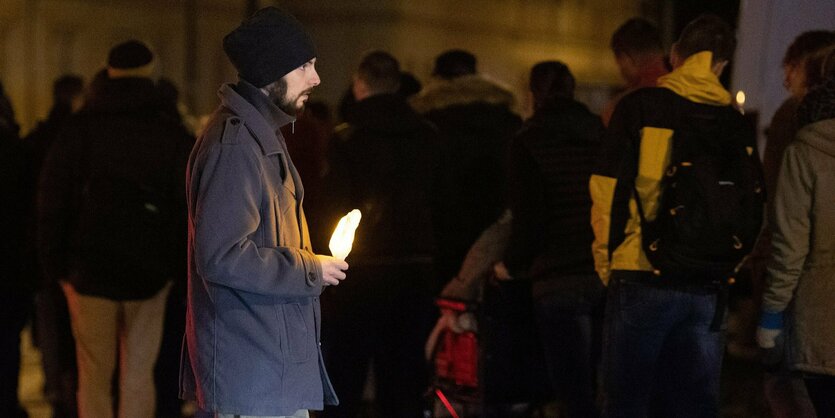 Ein junger bärtiger mann mit einer Kerze seitlich im Demonstrationszug