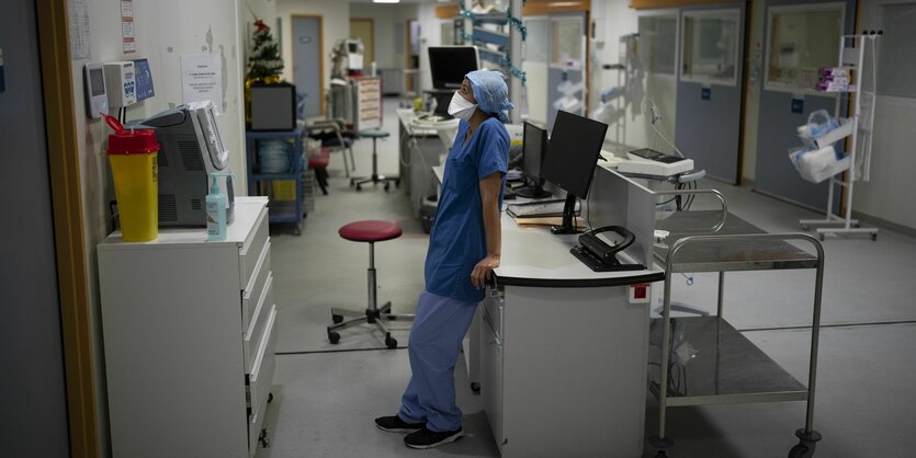 Eine Frau mit FFP-2-Maske und Schutzumhang schaut in einem Krankenhaus auf einen Bildschirm