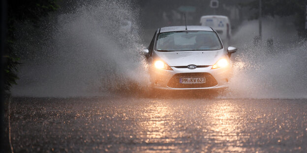 Ein Auto fährt bei unwetterartigem Niederschlag über eine überflutete Straße