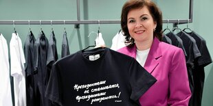 Eine Frau hält in einem Geschäft ein T-Shirt in die Kamera