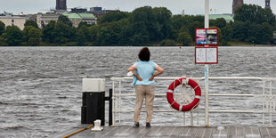 Eine Person steht an einem Anleger an der Alster und blickt aufs Wasser.