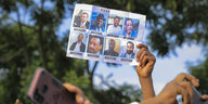 Eine Hand hält ein DinA-4-Blatt mit den Fotos von inhaftierten Oppositionellen und Rebellen in die Höhe