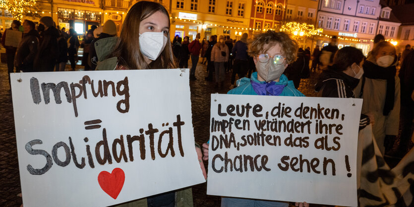 Peson mit Maske hält Schild mit der Aufschrift "Impfung = Solidarität"