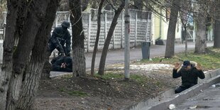 Ein bewaffneter Bereitschaftspolizist hält zwei Demonstranten während einer sogenannten Anti-Terror-Operation in einer Straße nach Zusammenstößen in Almaty, Kasachstan, fest.