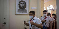 Schüler mit Mundschutz gehen an einem Bild von Che Guevara vorbei