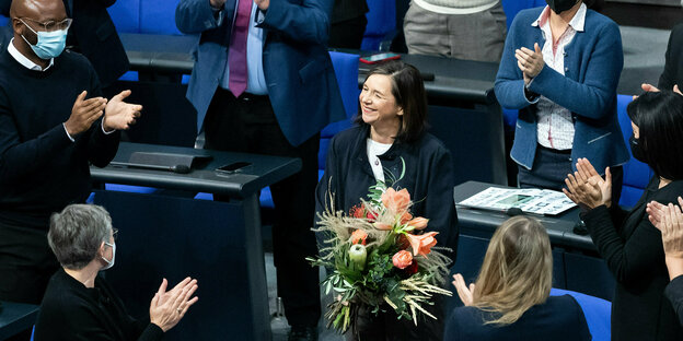 Katrin Göring-Eckhardt steht im Bundestag, hält einen Blumenstrauß in der Hand, lächelt und wird von Bundestagsabgeordneten beklatscht.
