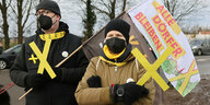 Zwei Demonstrant*innen mit gelben X-Symbolen